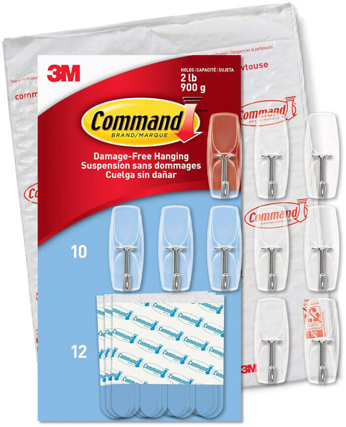 White Command hooks mounted inside cabinet door holding kitchen utensils and measuring cups