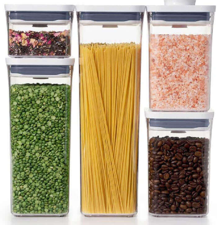 Clear square airtight containers lined up on pantry shelf holding flour, sugar, and pasta