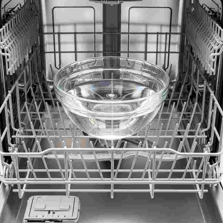 White vinegar in bowl on top rack of empty dishwasher for natural cleaning cycle